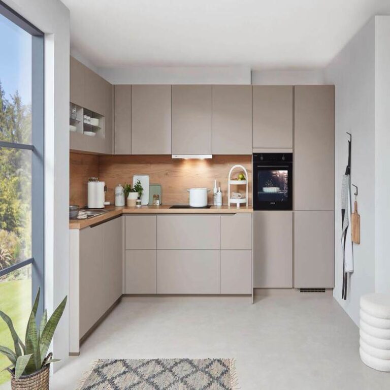 Musterküche in Kaschmir als L-Küche mit Holzrückwand und Backofen im Hochschrank – Küchenstudio Hagen